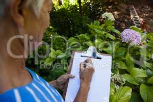 Midsection of senior woman writing on clipboard against plants