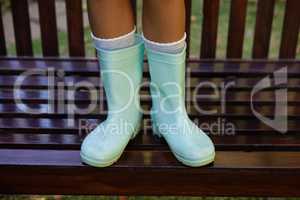 Low section of girl wearing green rubber boot standing on wooden bench