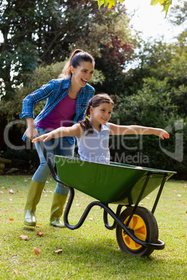 Cheerful mother pushing daughter sitting in wheelbarrow