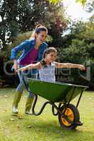 Cheerful mother pushing daughter sitting in wheelbarrow