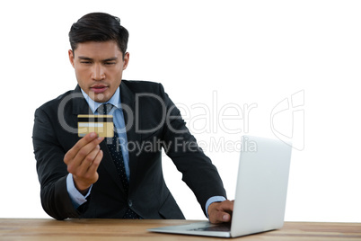Businessman holding credit card while using laptop