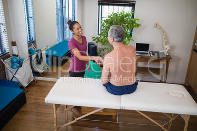 High angle view of smiling female therapist shaking hands with shirtless senior male patient sitting