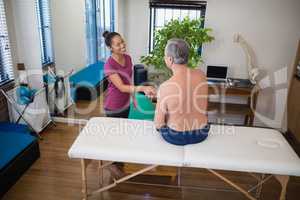 High angle view of smiling female therapist shaking hands with shirtless senior male patient sitting