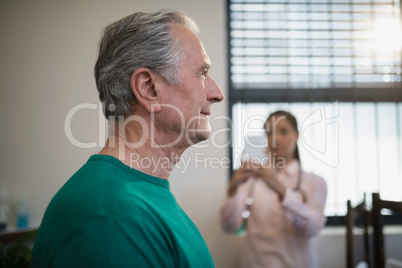 Side view of senior male patient with female therapist photographing against window