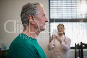 Side view of senior male patient with female therapist photographing against window