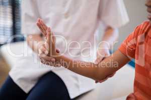 Midsection of female therapist examining wrist while boy sitting on bed