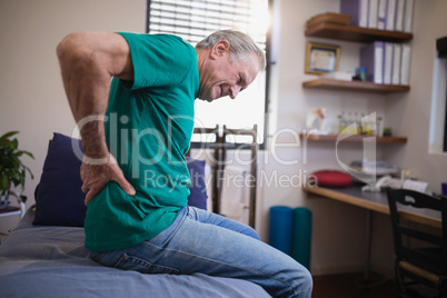 Side view of male patient grimacing from back ache while sitting on bed