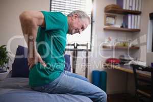Side view of male patient grimacing from back ache while sitting on bed