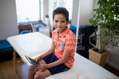 High angle portrait of smiling boy sitting with digital tablet on bed