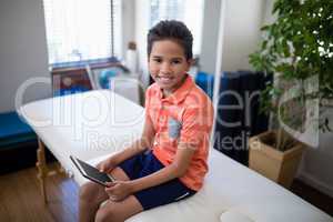 High angle portrait of smiling boy sitting with digital tablet on bed