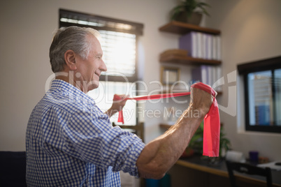 Side view of senior man pulling resistance band in hospital ward