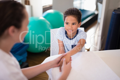 High angle view of smiling boy looking at female therapist examining hand