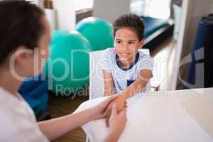 High angle view of smiling boy looking at female therapist examining hand