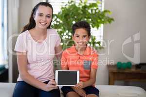 Portrait of smiling female therapist showing digital while sitting with arm around boy on bed