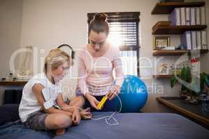 Female therapist showing electrical muscle stimulation machine to boy sitting on bed
