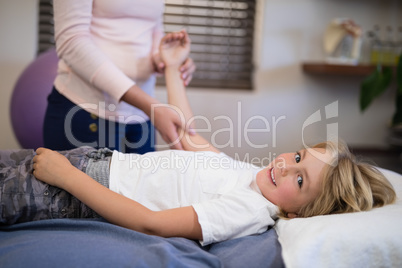 Portrait of smiling boy lying on bed while female therapist examining arm