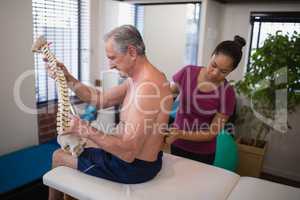 Female therapist examining back of shirtless male patient holding artificial spine