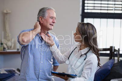 Female therapist examining neck of senior male patient