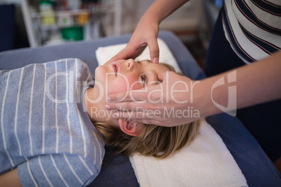 Midsection of female therapist giving head massage to boy lying on bed