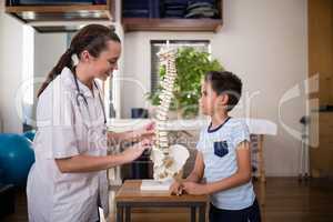 Side view of smiling young female therapist explaining to boy with artificial spine