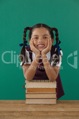 Schoolgirl leaning on books stack against chalkboard in classroom