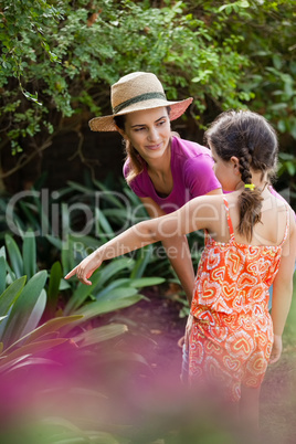 Woman looking at girl pointing while standing by plants