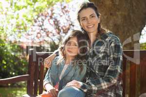 Portrait of smiling beautiful woman sitting with daughter on wooden bench