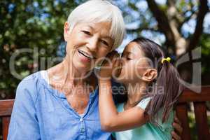 Girl whispering in ears of smiling grandmother