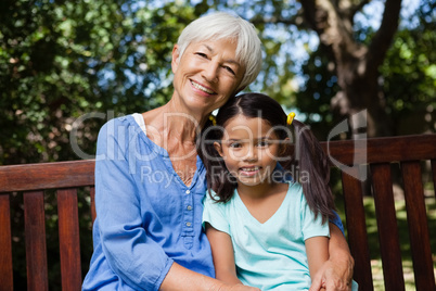 Portrait of smiling girl and grandmother sitting on wooden bench