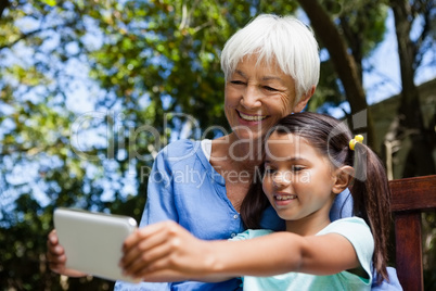 Smiling grandmother and granddaughter taking selfie while sitting on bench