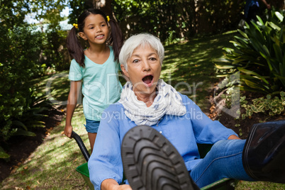 Girl pushing grandmother sitting in wheelbarrow