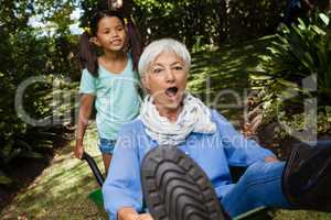 Girl pushing grandmother sitting in wheelbarrow