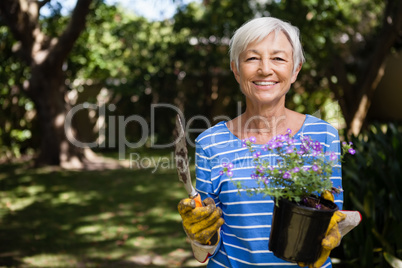 Portrait of senior woman holding potted plant and trowel