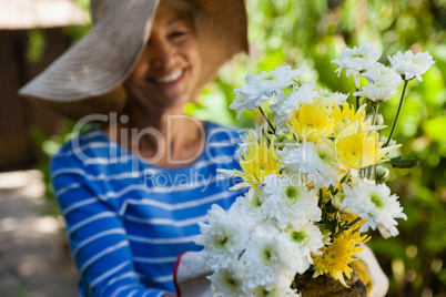 Smiling senior woman wearing hat holding fresh flowers
