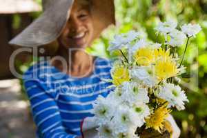 Smiling senior woman wearing hat holding fresh flowers