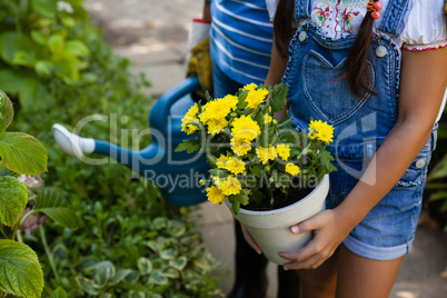 Midsection of senior woman and granddaughter holding watering can and yellow flower pot