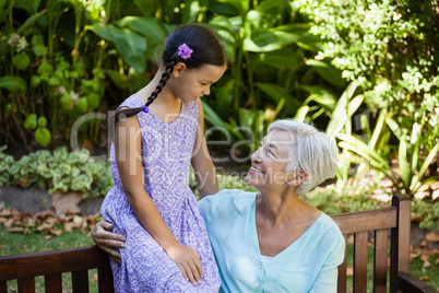 Smiling senior woman looking at girl while sitting on wooden bench