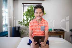 Portrait of smiling boy sitting with digital tablet on bed