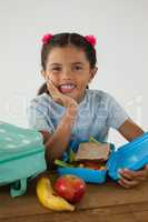 Schoolgirl sitting with tiffin box against white background
