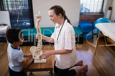 Side view of smiling female therapist explaining boy with artificial spine