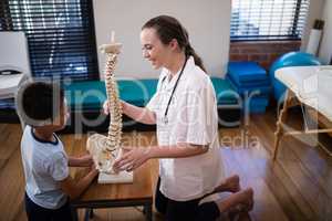 Side view of smiling female therapist explaining boy with artificial spine