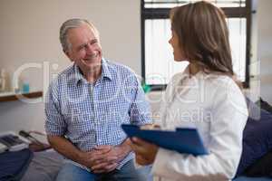 Smiling senior male patient looking at female therapist with file
