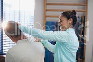 Smiling female therapist examining neck of senior male patient