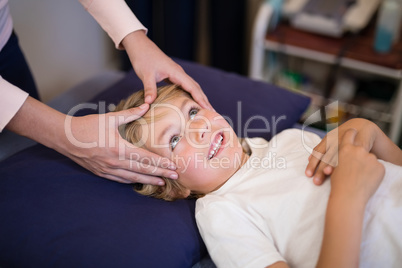 Cropped hands of female therapist giving head massage to boy lying on bed