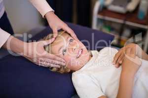 Cropped hands of female therapist giving head massage to boy lying on bed