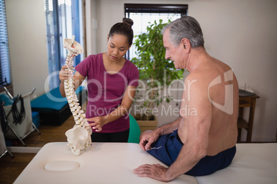 Female therapist explaining shirtless senior male patient with artificial spine