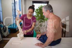 Female therapist explaining shirtless senior male patient with artificial spine