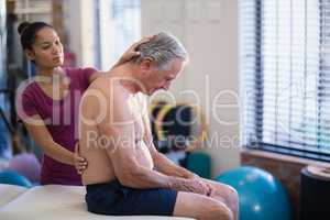 Young female therapist giving back massage to senior male patient sitting on bed
