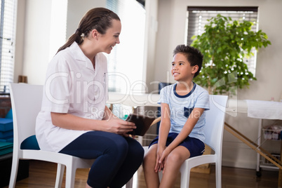 Smiling boy and female therapist sitting with digital tablet