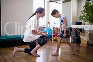 Boy showing knee to female therapist kneeling on hardwood floor